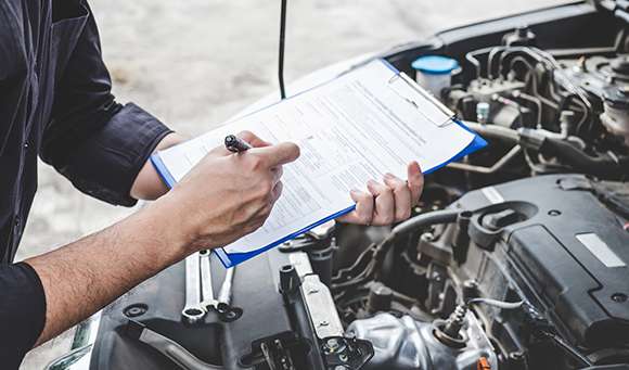 a man with a clipboard assessing an engine of a car under the bonnet