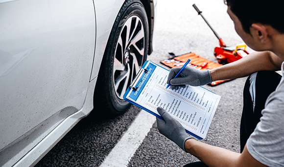 a man with a checklist on a clipboard assessing the tyres of a car