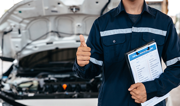 a man with a clipboard giving a thumbs up in front of a car with it's bonnet up