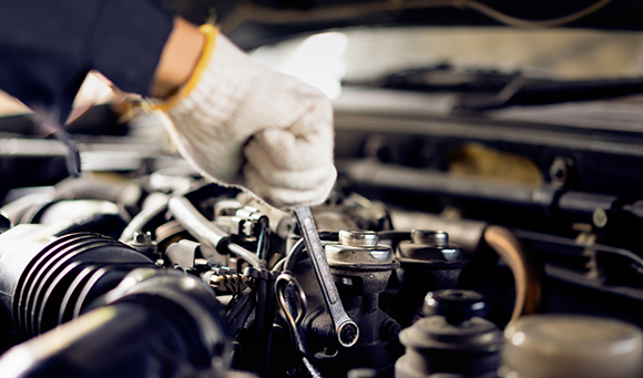 a gloved mechanic using a wench to bolt a part of a car engine in place